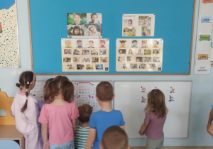 Dzieci znajdują się na tle tablic z planszami demonstracyjnymi o emocjach