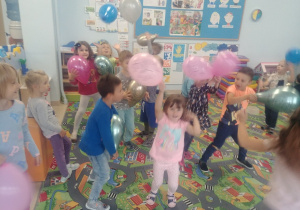 Dzieci z grupy Niebieskiej tańczą z balonami do muzyki dynamicznej w swojej sali.