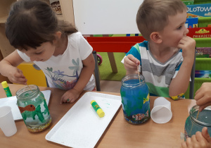 Dziewczynka i chłopiec barwią wodę w swoich słoikach.