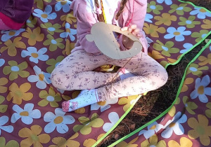 Dziewczynka siedzi i nawleka nitkę w kartonowego żołędzia.