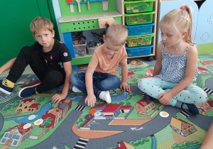 Dzieci siedzą na dywanie i tworzą obrazek z kropek.