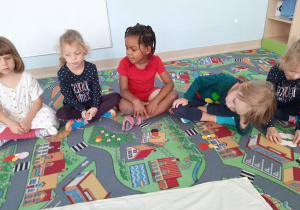 Dzieci siedzą na dywanie i układają obrazek z kropek.