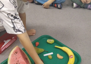 Chłopiec dopasowuje napis do owocu ułożonego na dużej tacy.