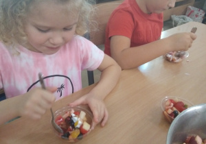 Dziewczynka i chłopiec siedzą przy stole i konsumują sałatkę owocową.