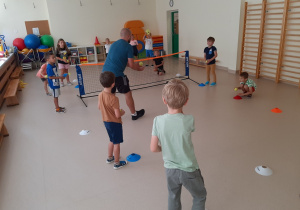 Dzieci, trzymając w rękach piłki tenisowe słuchają instrukcji trenera.