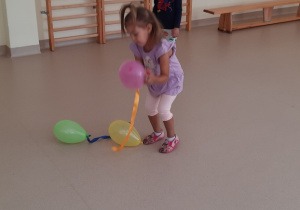 Dziewczynka bawi się balonami, chłopiec obserwuje jej zabawę.