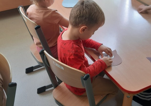 Dzieci siedzą przy stoliku i wykonują papierową sowę.