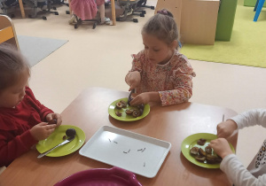 Trzy dziewczynki siedzą przy stoliku i usuwają pestki ze śliwek.