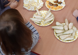 Dzieci siedząc przy stoliku degustują owoce