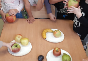 Dzieci stoją przy stoliku trzymając owoce w ręku
