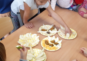 Dzieci jedzą owoce , na stoliku pokrojone są owoce