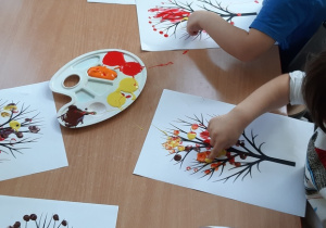 Dzieci robią paluszkowe stempelki z farby na kartce papieru, które przedstawia drzewo