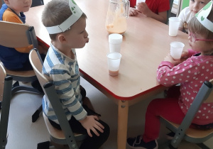 Grupka dzieci przy stoliku pije sok z kubeczków