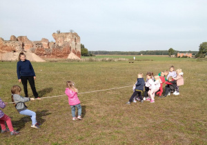 Grupa dzieci w zawodach przeciągania liny. W tle widoczne ruiny zamku.