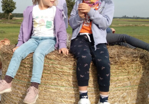 Dwie dziewczynki siedzą na wysokiej beli siana.