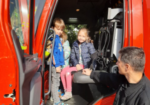Chłopiec i dziewczynka pozują do zdjęcia, siedząc w kabinie wozu strażackiego.