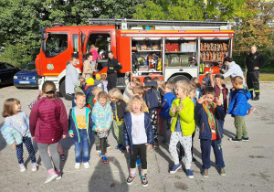 Grupa dzieci pozuje do zdjęcia na tle wozu strażackiego.