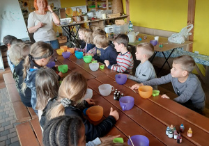 Dzieci siedzą przy długim stole, przygotowując produkty do robienia mydełek glicerynowych