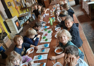 Dzieci siedzą przy długim stole i jedzą zupę pomidorową