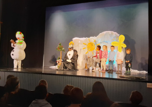 Dzieci stoją na scenie teatru, obok nich 2 aktorów