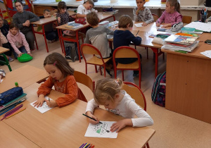 Dzieci siedzą w ławkach szkolnych i kolorują kolorowankę według podanego kodu