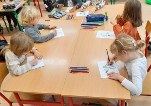 Dzieci siedzą w ławkach szkolnych i kolorują kolorowankę według podanego kodu