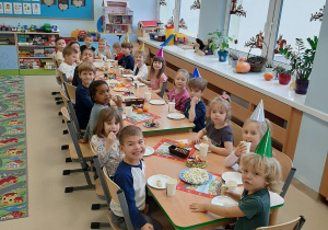 Dzieci siedzą przy długim stole z poczęstunkiem