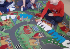 Dzieci siedzą na dywanie z papierowymi bałwankami