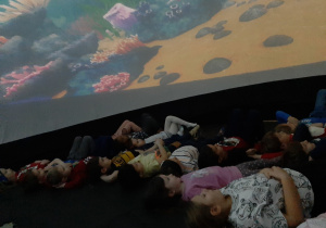 Dzieci leżą w środku Kina Sferycznego i oglądają bajkę