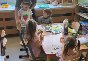 Dzieci siedzą przy stolikach i wykonują wiosenne prace plastyczne