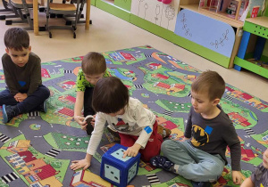 Dzieci siedzą na dywanie i liczą kropki na kostce