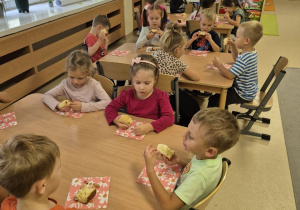 Dzieci siedzą przy stolikach i jedzą ciasto.