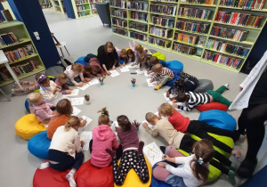 Dzieci siedząc lub leżąc na poduszkach, kolorują liście