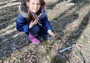 Dziewczynka wrzuca do słoika liście, szyszki, żołędzie itp, tworząc Las w słoiku