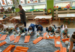 Dzieci siedzą na podłodze i rozwiązują kartę pracy.