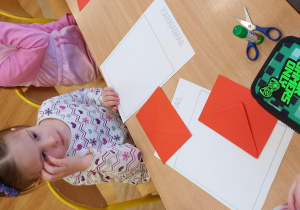 Dwie dziewczynki siedzą w ławce. Na ławce leżą białe kartki i czerwone koperty.