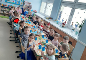 Dzieci siedzą przy długim stole z poczęstunkiem.