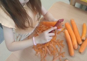 Dziewczynka obieraczką obiera marchewkę.