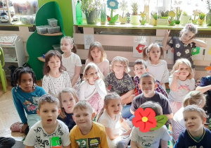 Dzieci siedzą na dywanie i oglądają występy dzieci.
