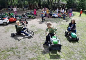 Troje chłopców siedzi na mini pojazdach, w tle reszta grupa dzieci