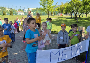 Grupa dzieci kibicuje biegnącym kolegom.