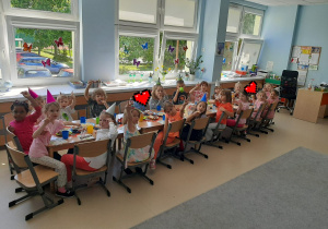 Dzieci siedzą przy długim stole i pozują do zdjęcia.