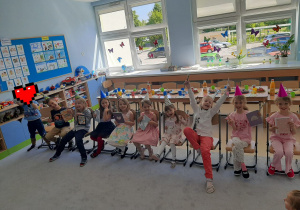 Jubilaci siedzą na krzesłach i pokazują prezenty.