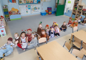 Dzieci przebrane w stroje jesienne siedzą na dywanie