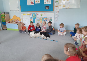 Dzieci siedzą na dywanie i głaszczą psa.