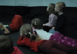 Dzieci leżąc na podłodze oglądają seans filmowy.