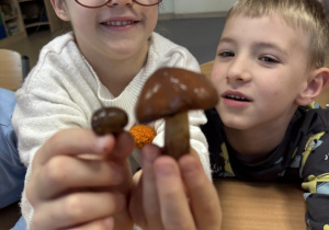 Dziewczynka trzyma w dłoniach małego i dużego grzyba maślaka.