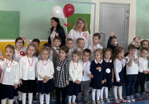 Dzieci ubrane w stroje galowe stoją w szeregu przed odśpiewaniem wspólnie ze społecznością szkolną hymnu państwowego.