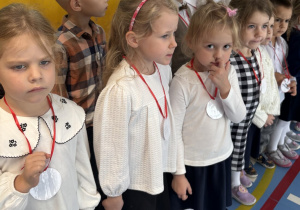 Dzieci ubrane w stroje galowe ustawiają się do odśpiewania ze społecznością szkolną hymnu państwowego.