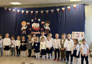 Grupa dzieci stoi na środku sceny i śpiewa pieśń patriotyczną.